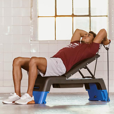 Model doing incline bench triceps work on the blue Reebok Deck