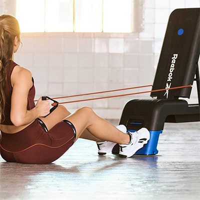 Model doing seated row with resistance tubes on the blue Reebok Deck