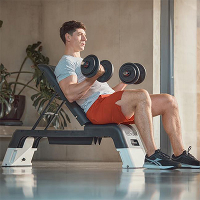 Model doing seated dumbbell curls on the white Reebok Deck