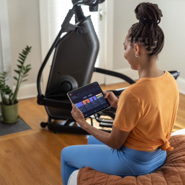 Model selecting a workout on a tablet app near the Schwinn 590E Elliptical