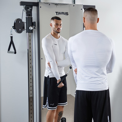 Lifestyle image of a model using the Taurus Design Line Dual Pulley for a tricep extension exercise. 