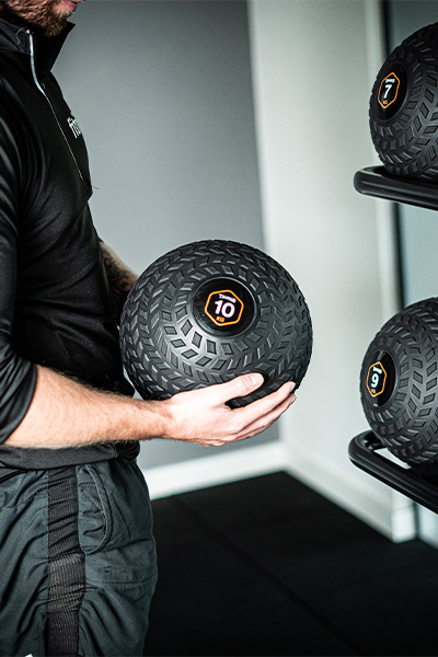 User holding 10 kg slam ball next to rack