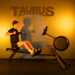 User rowing on the Taurus RX7 Rowing Machine with Taurus branding in the background.
