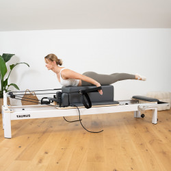 Model performing a prone Pilates back extension on the box of the Taurus Pro Pilates Reformer