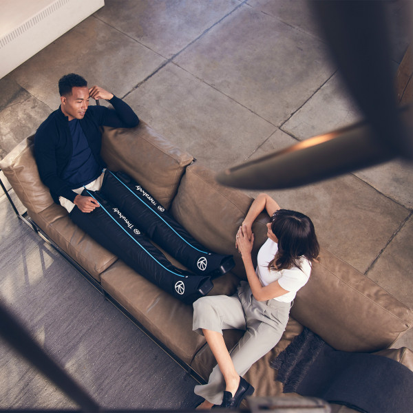 Overhead view of two people conversing while using Therabody RecoveryAir JetBoots.
