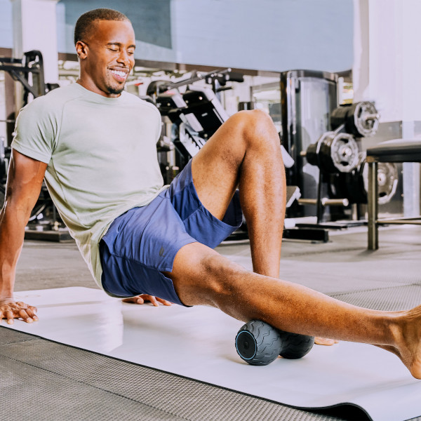 A person applying the Theragun Wave Duo to their calves for muscle recovery in the gym.
