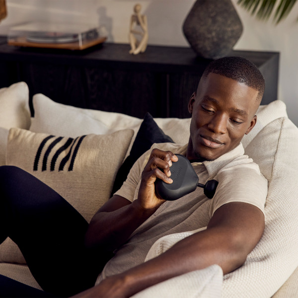 Theragun Mini 2.0 with a model on a sofa massaging their shoulder