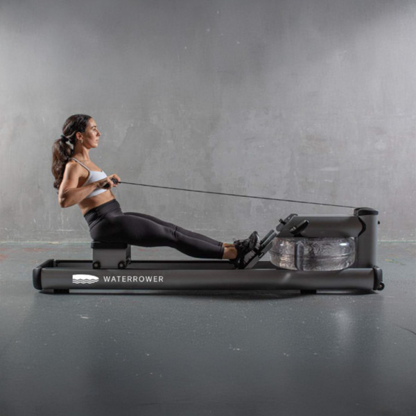 Lifestyle side view of a person using the WaterRower M1 LoRise Rowing Machine in black