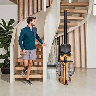 Model standing beside the WaterRower Hybrid Rowing Machine stored upright 